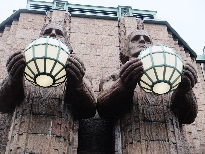 Two statues of mythical giants or gods holding spherical lamps stand welcoming travelers into the station.